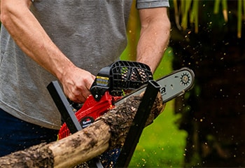 Homem usando uma motosserra da Toyama para cortar um pedaço de tronco de árvore.
