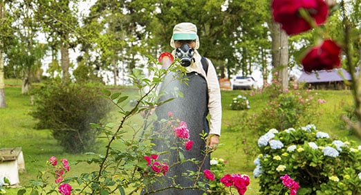 jardineiro equipado com EPIs realizando o controle de pragas em um jardim