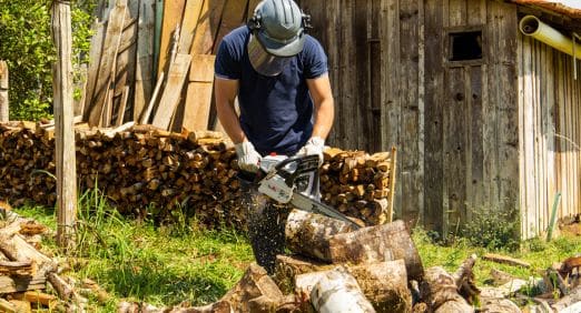 Homem usando uma motosserra da Toyama para cortar madeira em uma propriedade rural.